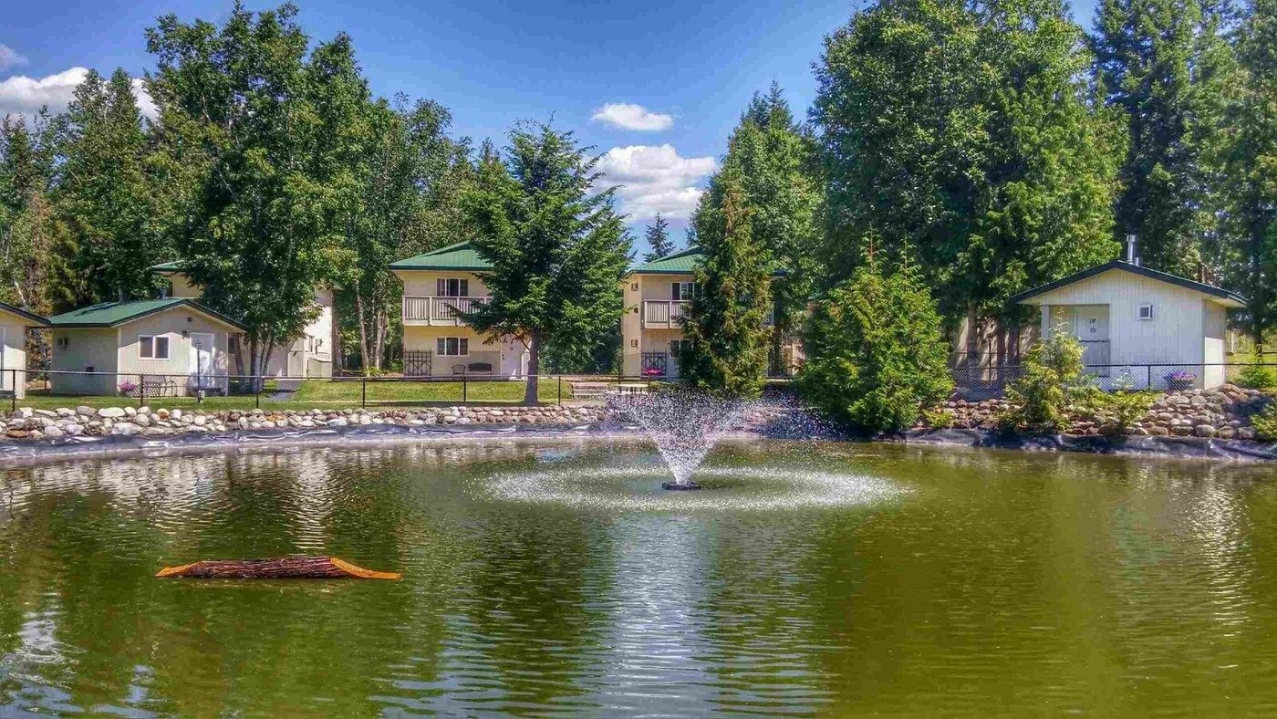 A pond with a fountain in front of lodging buildings among tall trees