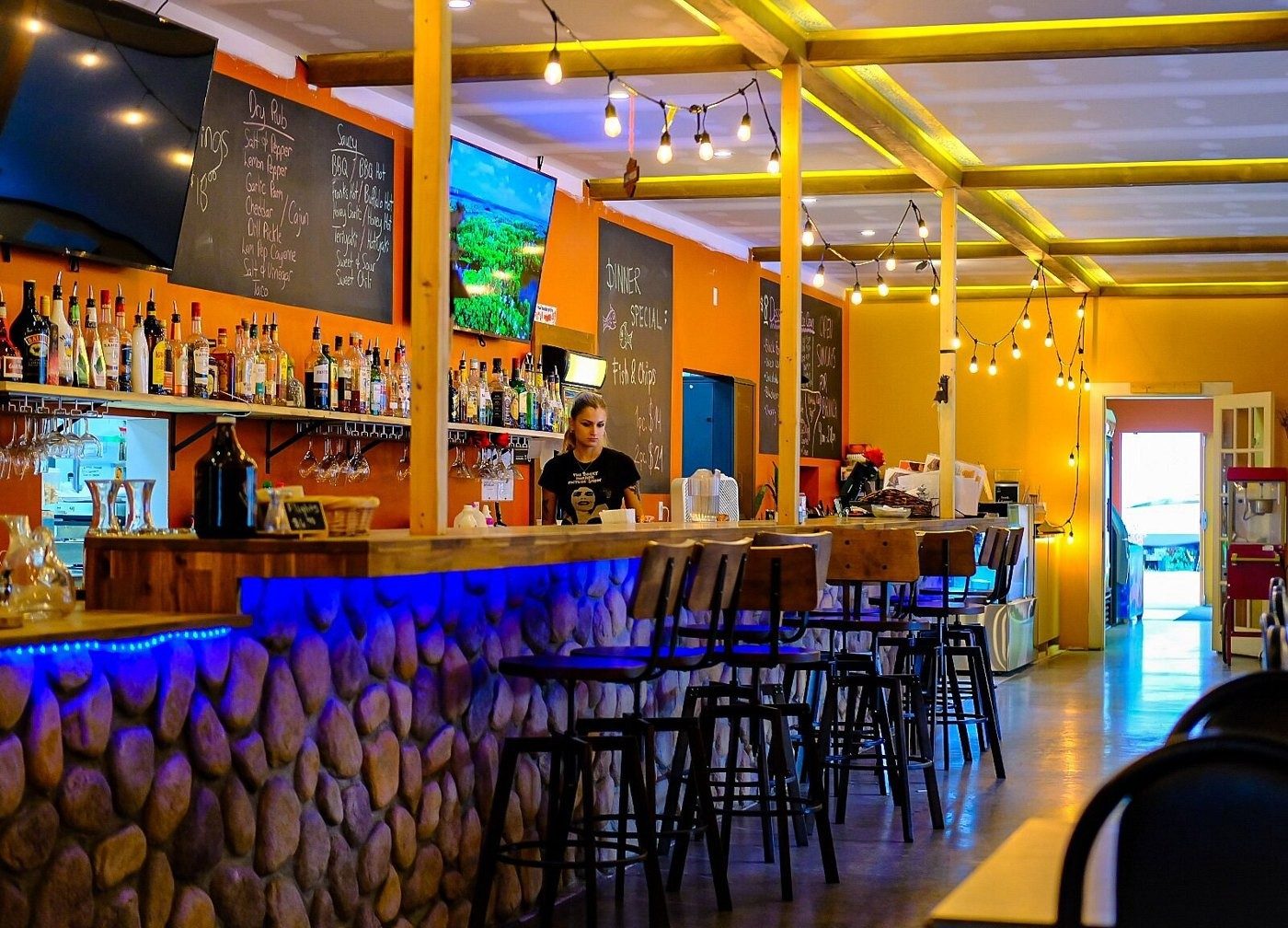 A warmly lit restaurant bar with stools and a chalkboard menu