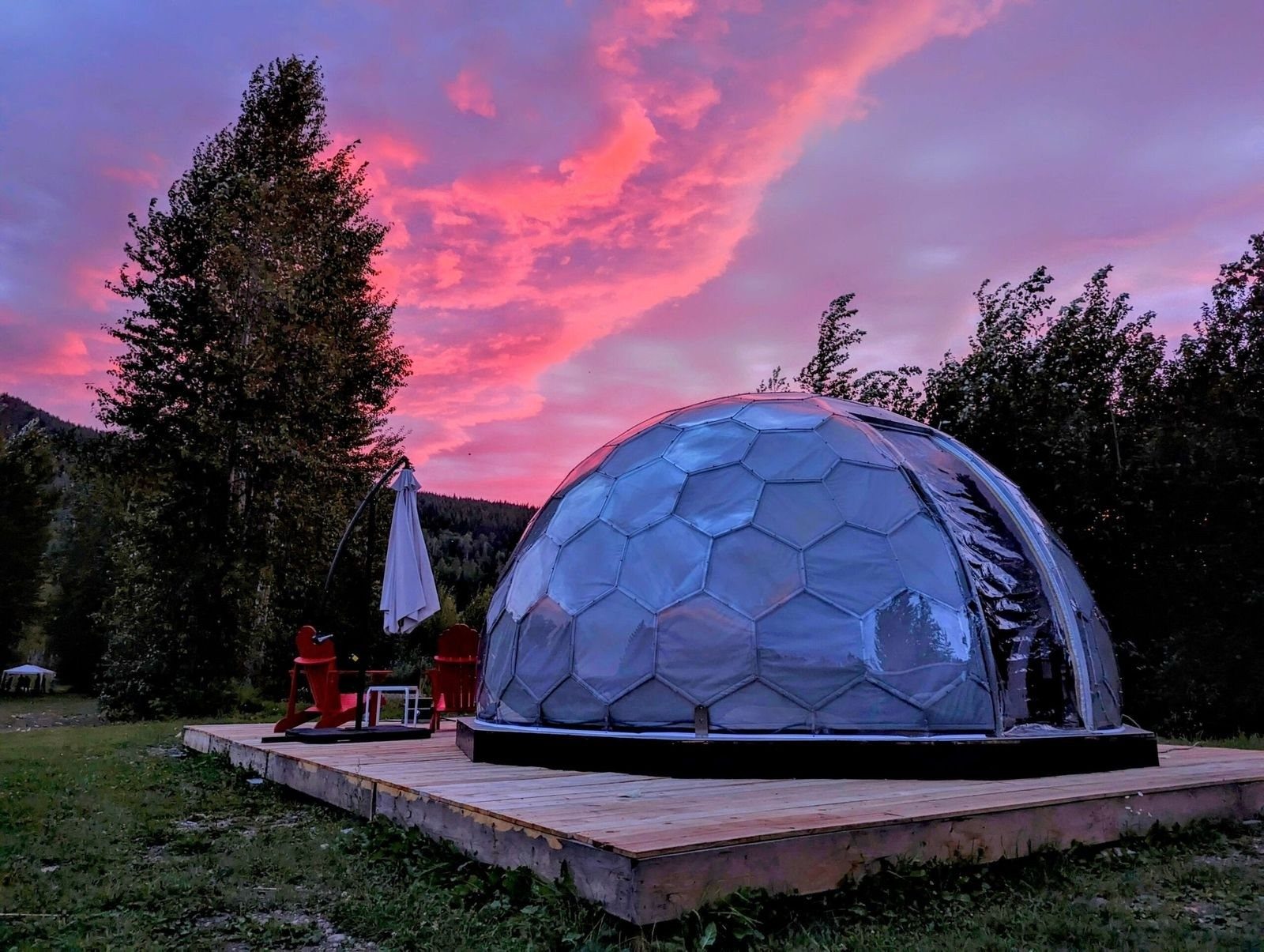 A geodesic dome on a timber deck under a pink and violet evening sky