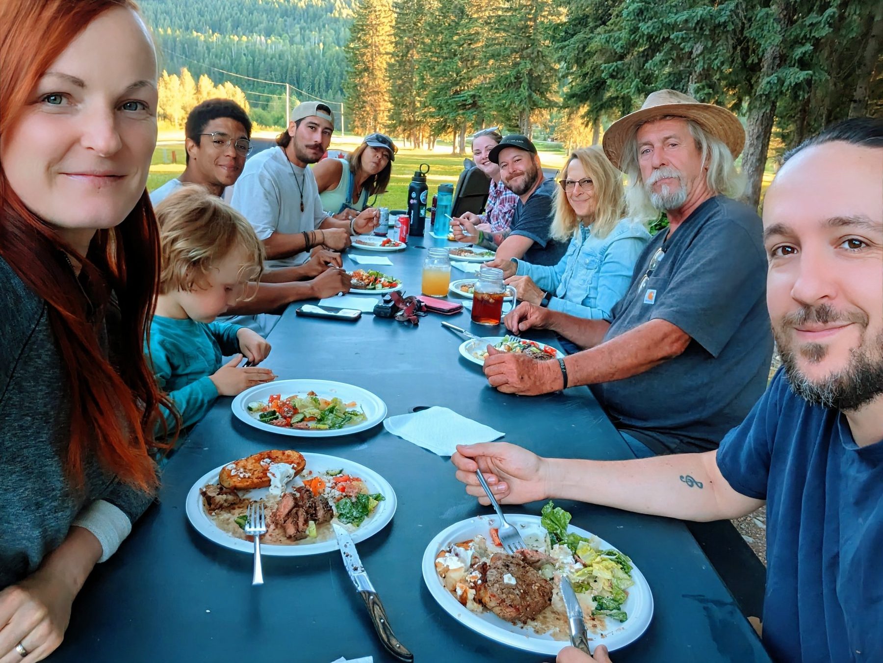 Families and friends around a long outdoor table loaded with food