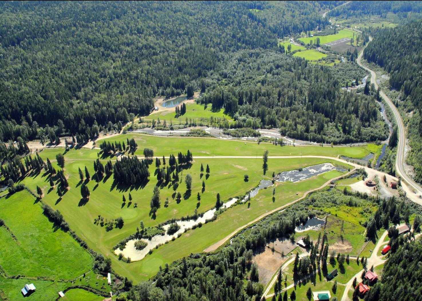 Aerial view of a green valley floor with a winding river and forested mountains, Wells Gray Resort below